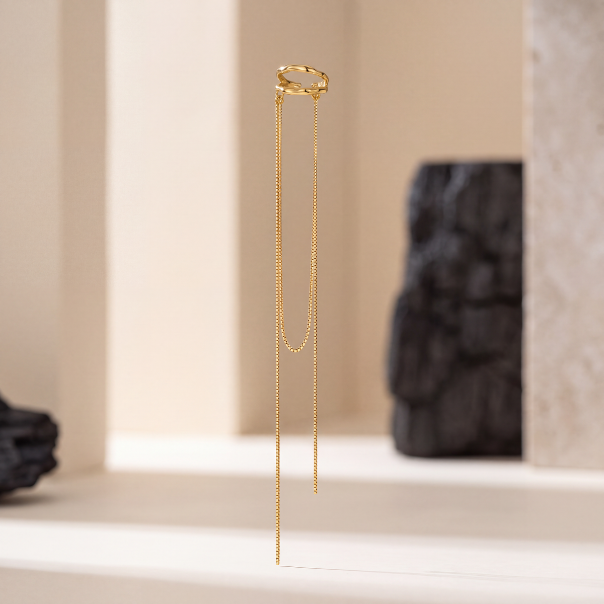 Golden Rain Ear Cuff in 18K gold plated 925 sterling silver, a bamboo-textured double hoop with two box chain tassels, standing against a cream wall with black stone, no piercing needed - Kavati
