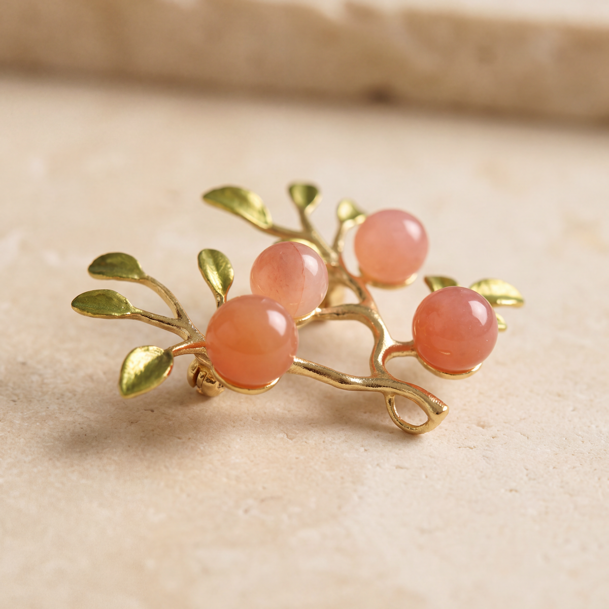 Angled close up of the Peach Orchard Branch Brooch, gold plated brass with natural red agate beads and green enamel leaves