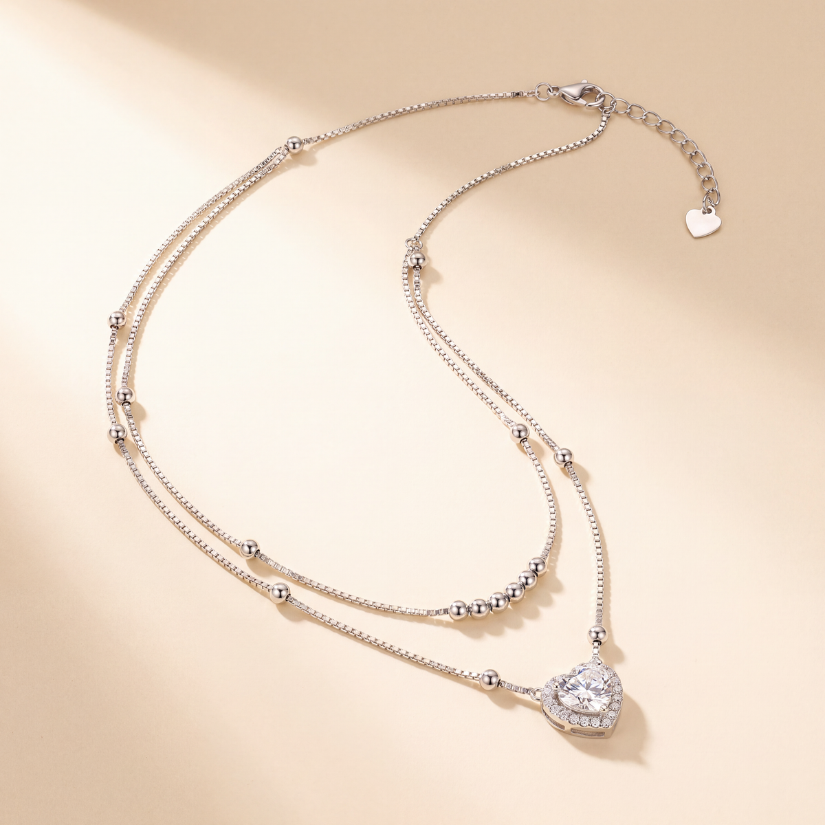 Juliet layered moissanite heart necklace in sterling silver, flat lay showing double box chain, silver beads and 1 carat heart pendant